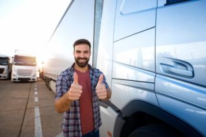 Truck driver holding two thumps up next to his truck